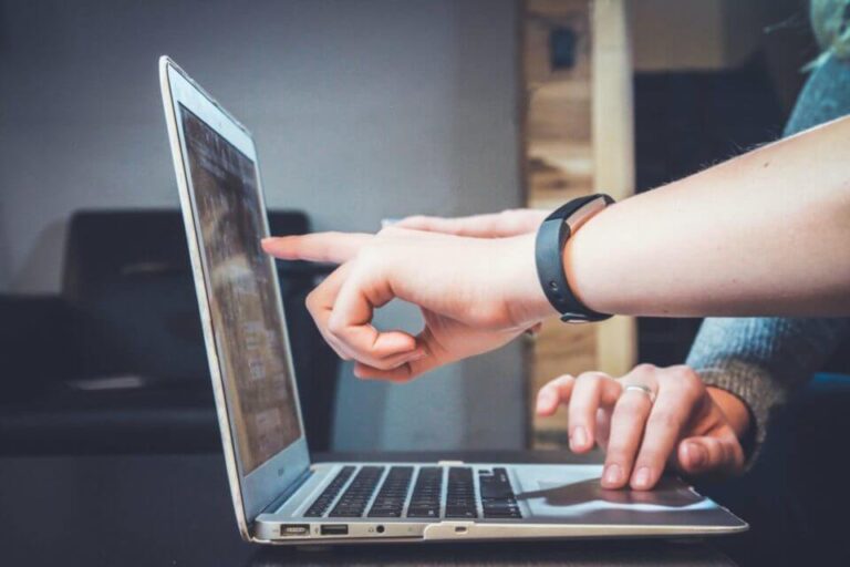 hand pointing at a laptop as people work